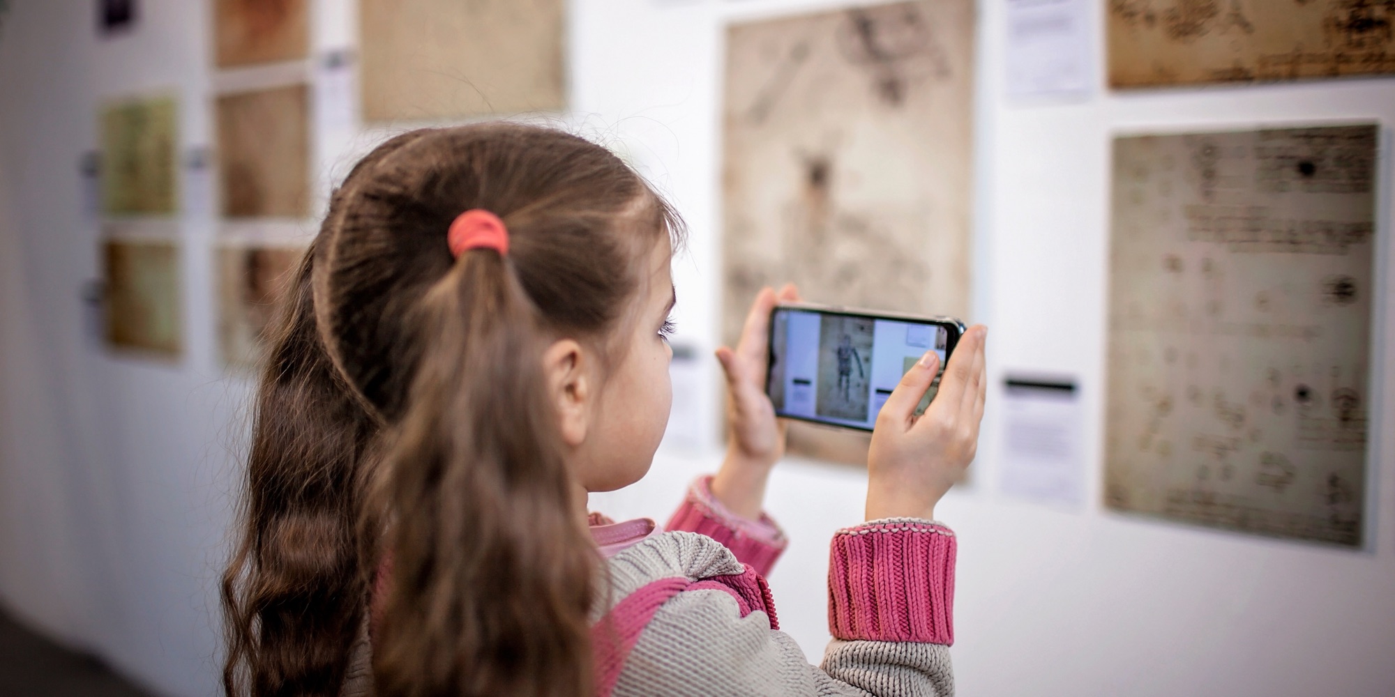 A young girl in a gallery photographing an exhibit on her smartphone