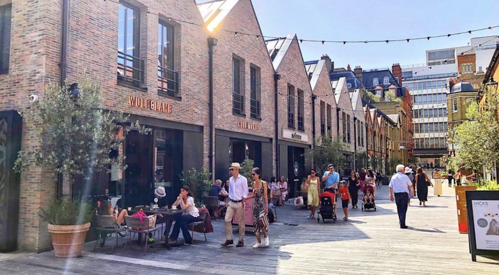 A busy pedestrian street of shops and café tables on a sunny day